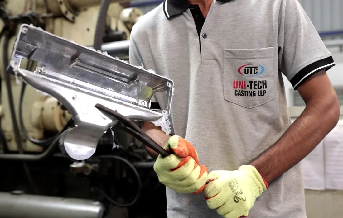 worker wearing safety gloves inspecting die-cast component